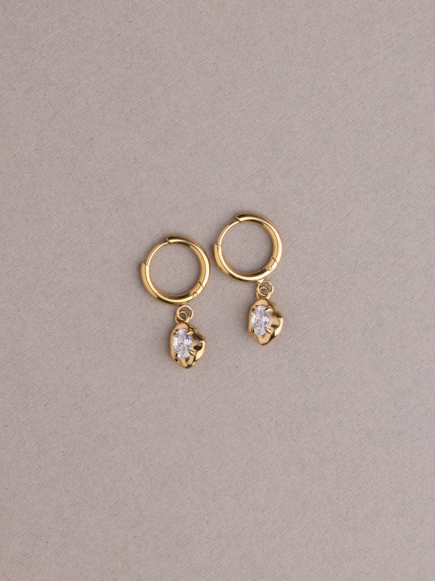 Gold hoop earrings with heart-shaped gemstones on a beige background
