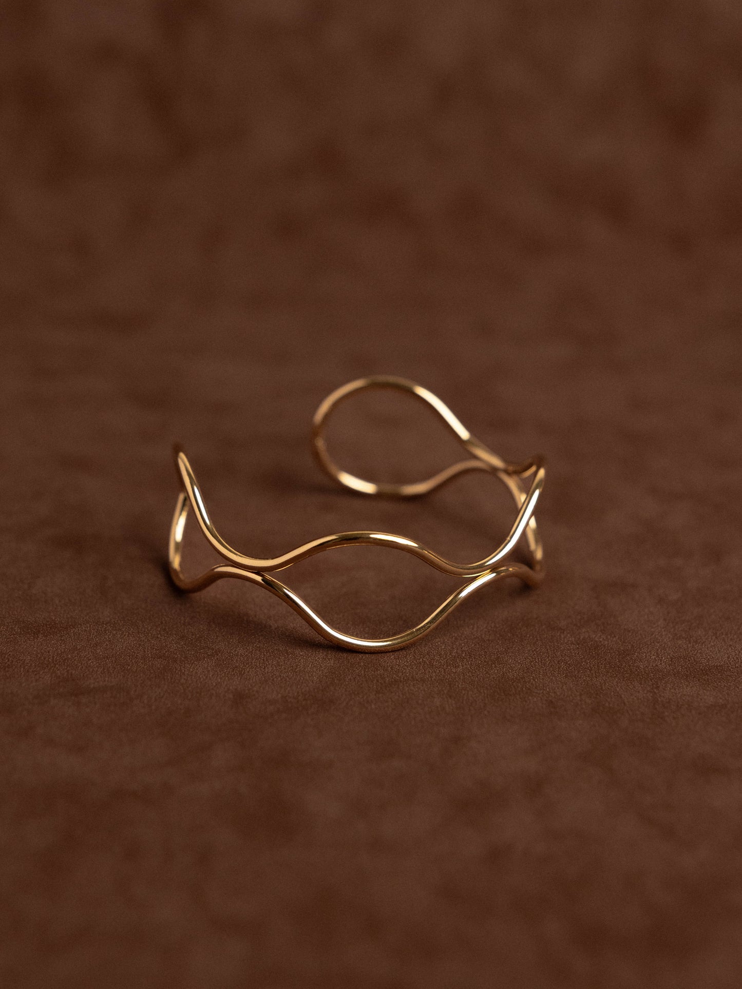 Gold open ring with wavy design on a brown textured background