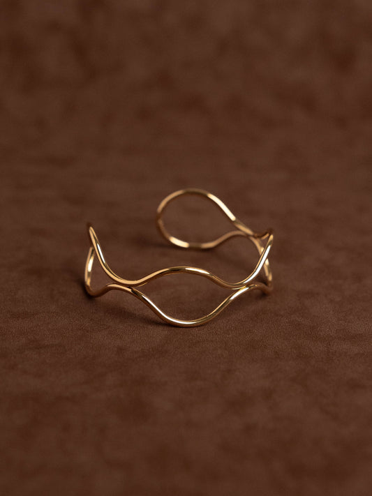 Gold open ring with wavy design on a brown textured background