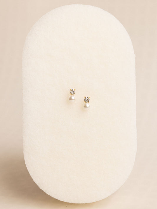 Pair of pearl earrings on a white oval stand against a beige background