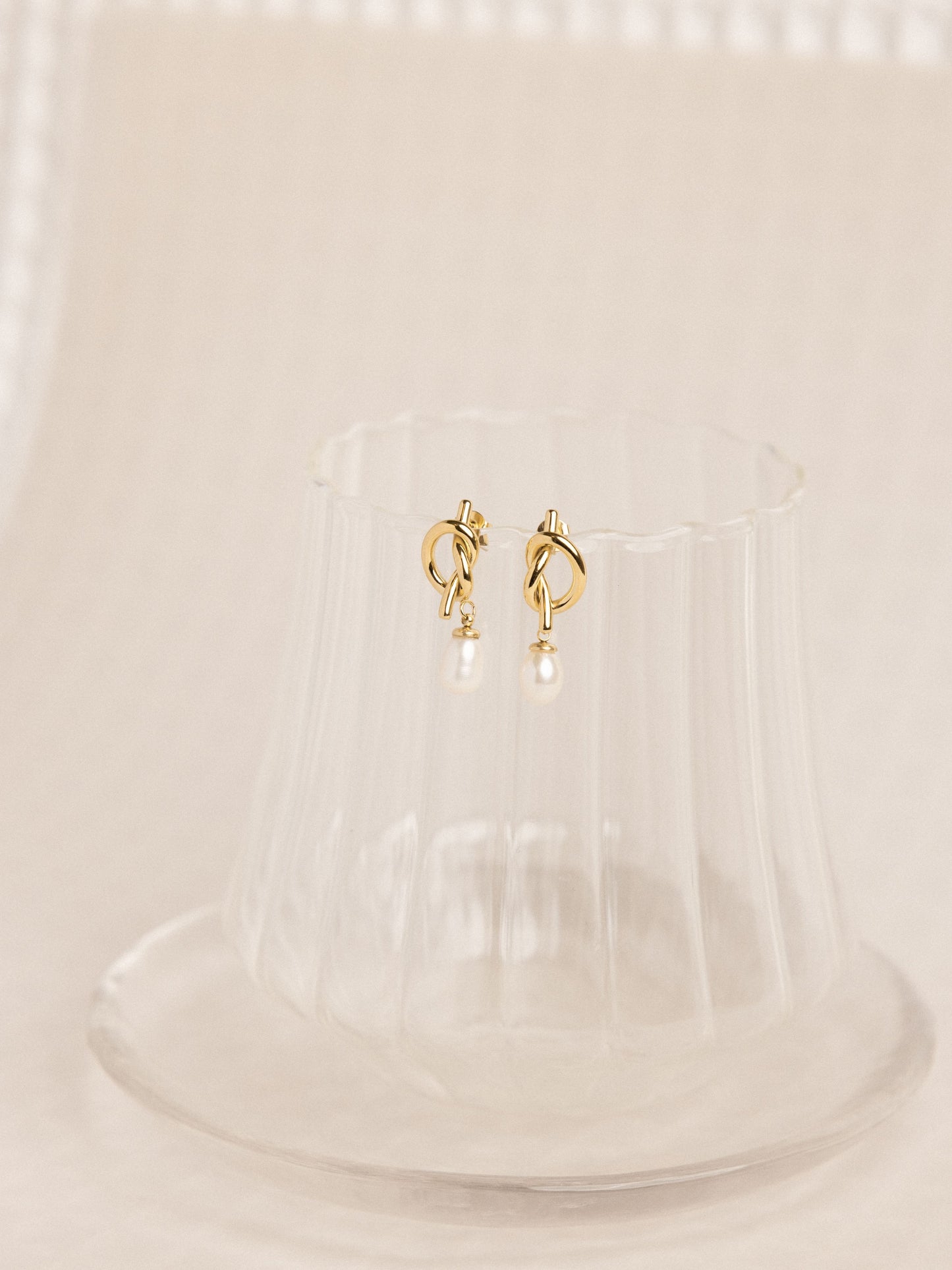 Gold hoop earrings on a clear stand with a beige background