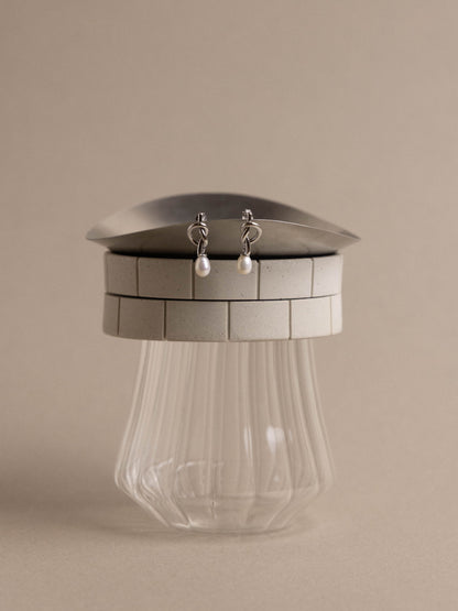 Silver earrings displayed on a metallic stand with a clear glass base against a beige background