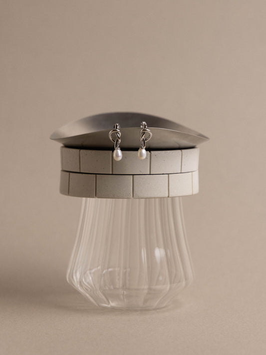 Silver earrings displayed on a metallic stand with a clear glass base against a beige background