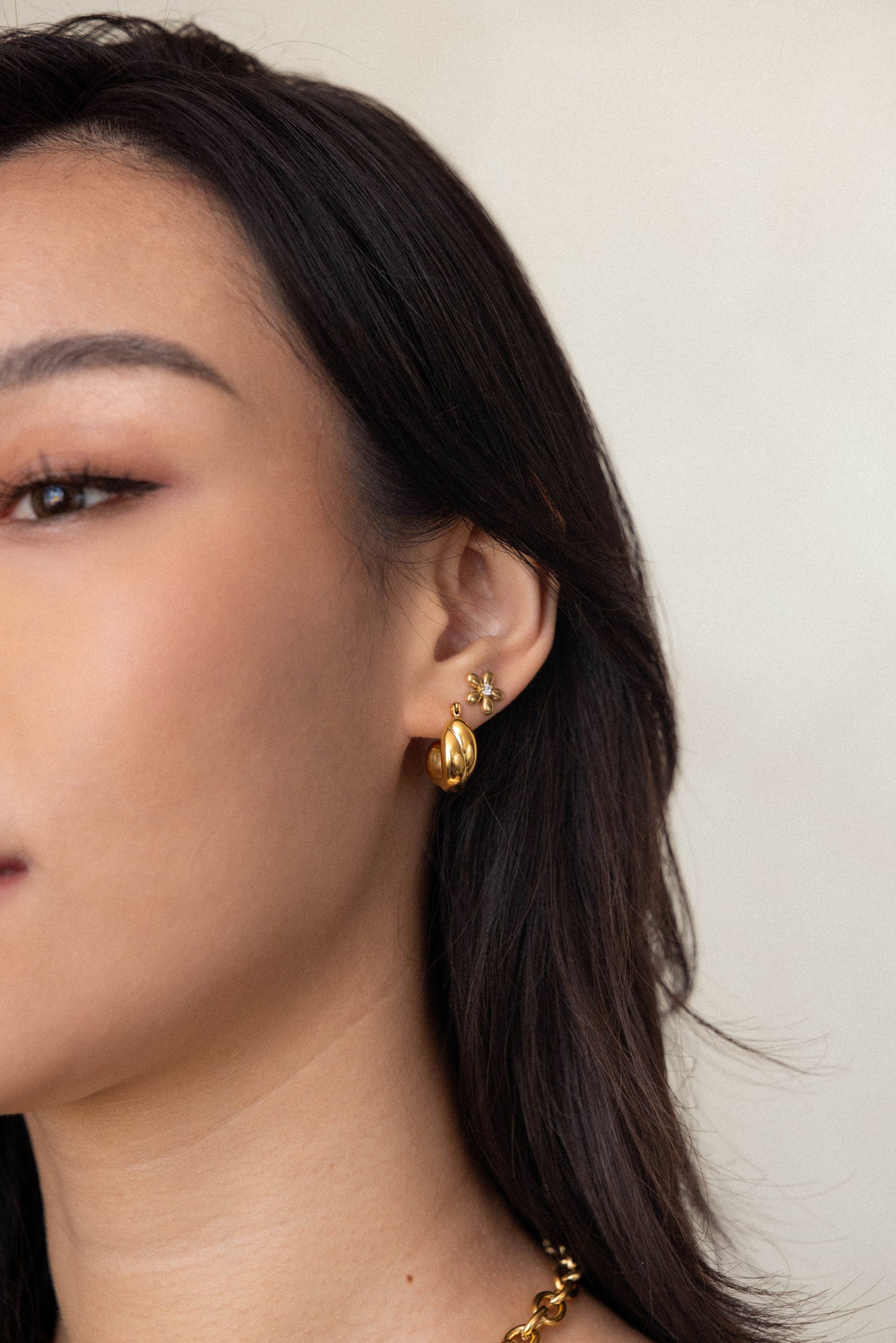 Close-up of a person wearing gold earrings with a neutral background