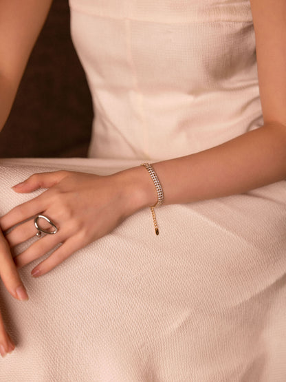 Close-up of a hand wearing a ring and bracelet on a soft pink fabric background