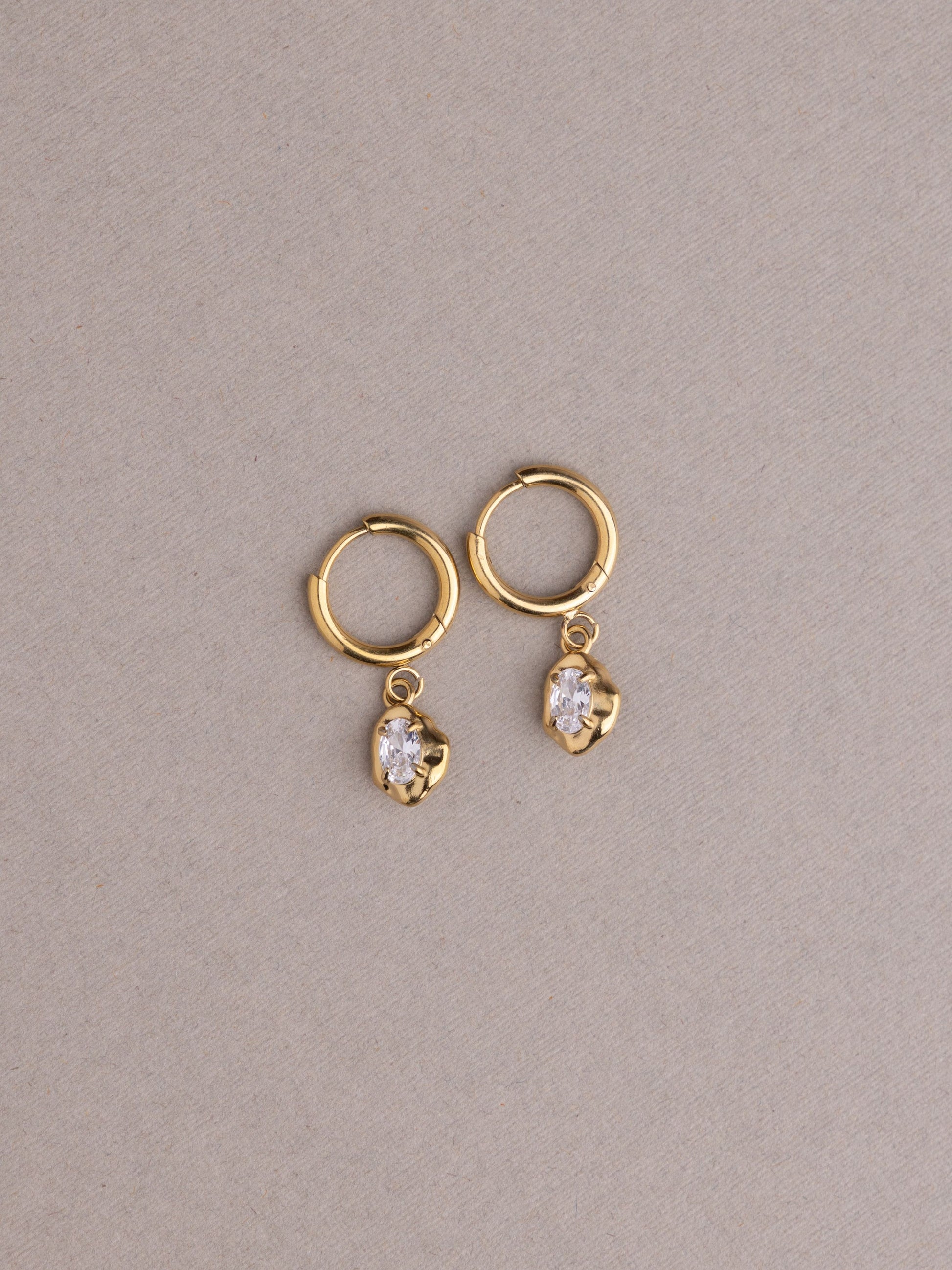 Gold hoop earrings with heart-shaped gemstones on a beige background