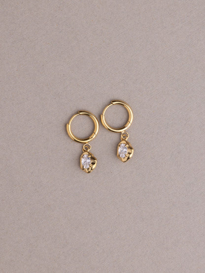 Gold hoop earrings with heart-shaped gemstones on a beige background