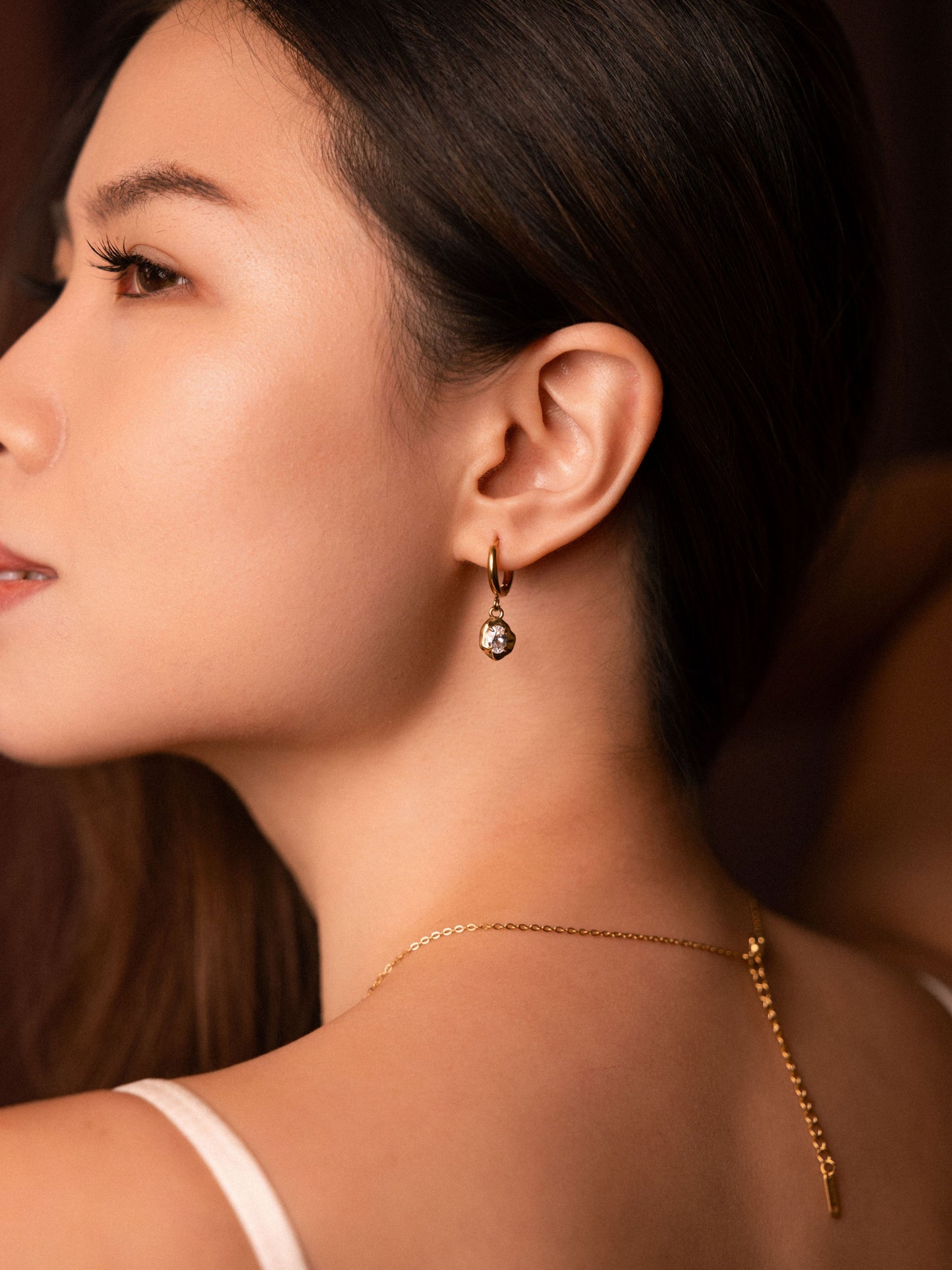 Close-up of a woman wearing gold earrings and a necklace against a blurred background