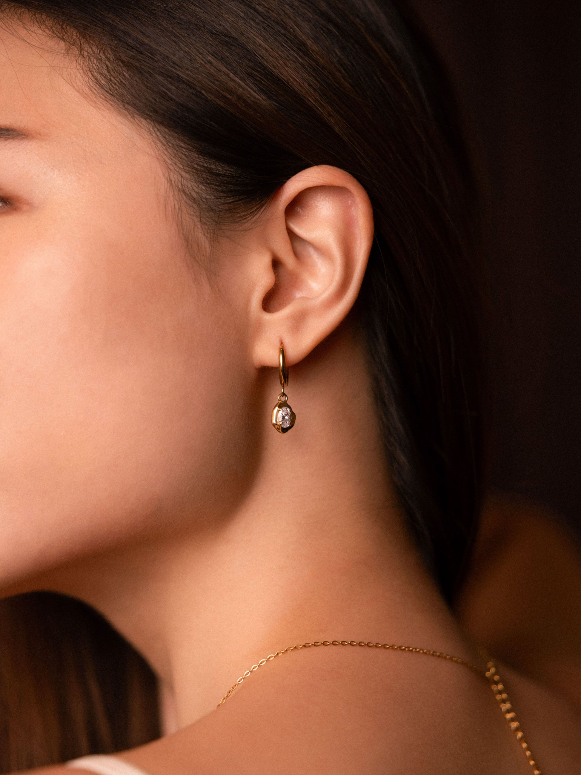 Close-up of a person wearing gold earrings with a blurred background